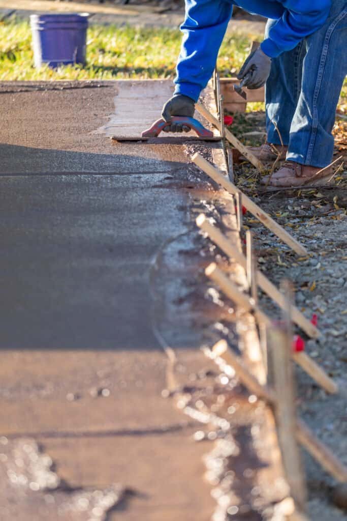 Concrete being leveled and smoothed during landscaping work by a worker.